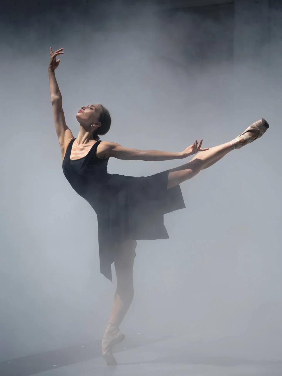 Zuzanna Kidziak holding an extended ballet line in a mist-filled Paris space